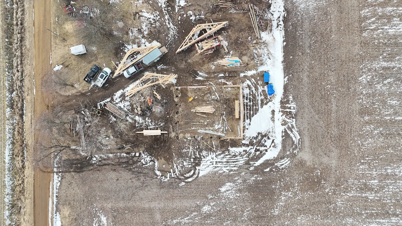 Owosso barn build — overhead site view, framing materials staged, winter documentation