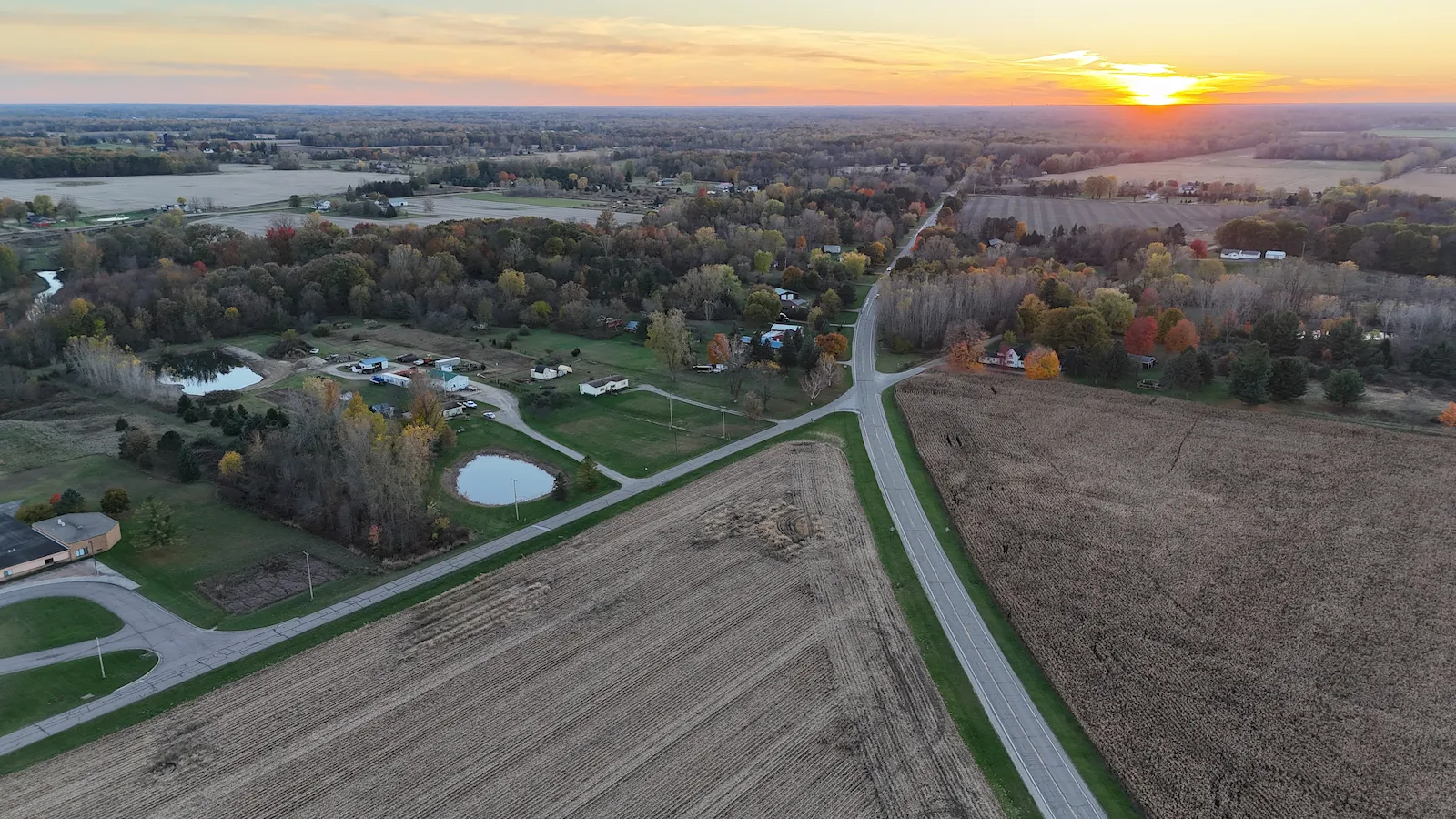 Rural Michigan landscape at sunset — fields, ponds, and country roads from above